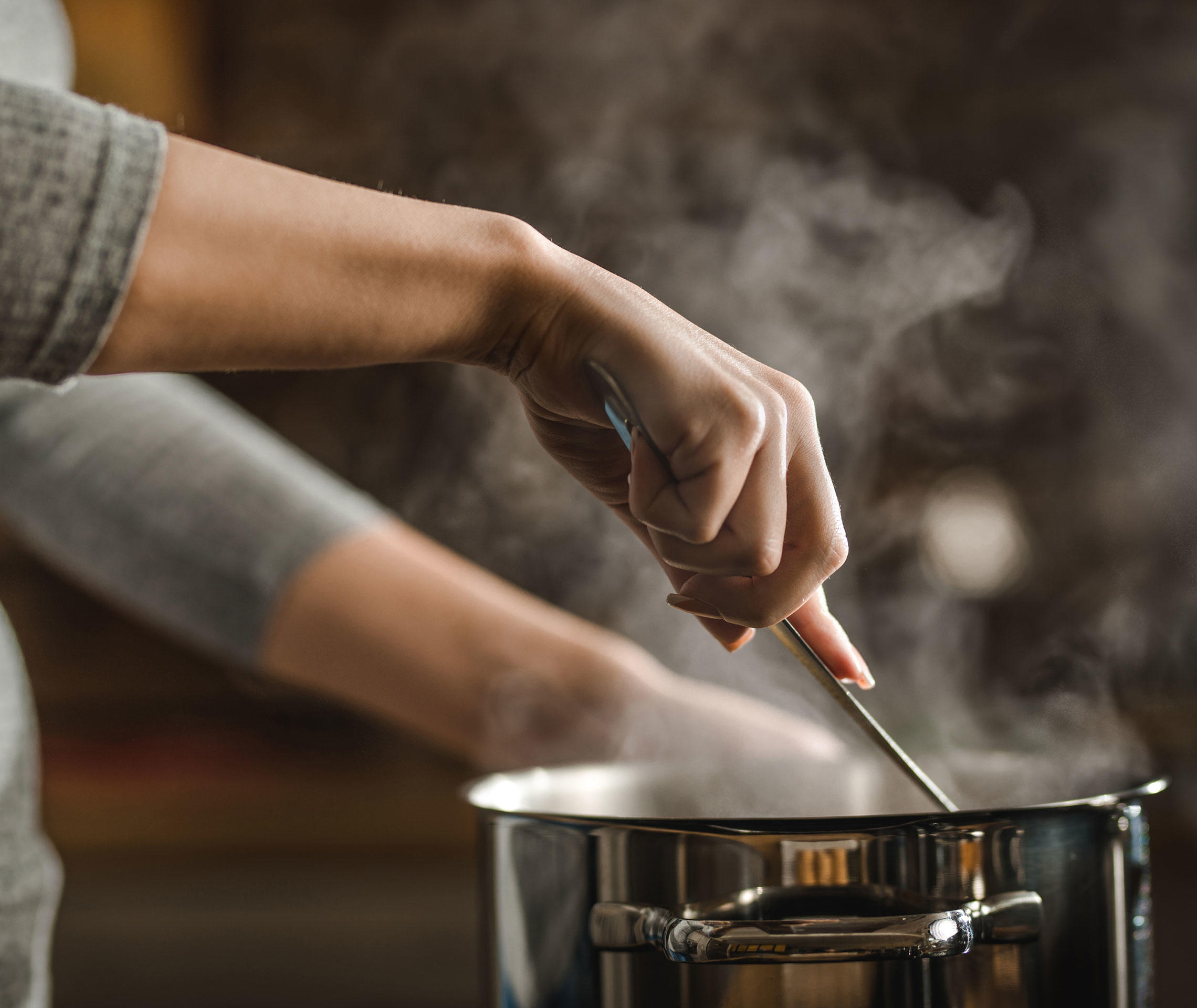 Frau mit Kochtopf beim Kochen mit Kochlöffel.