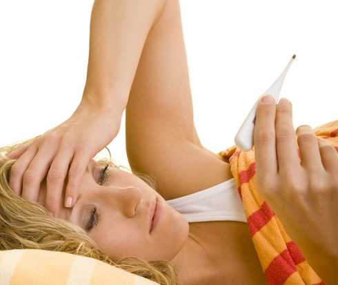 Eine Frau liegt mit Bett, fühlt mit der einen Hand ihre Strin und schaut auf einn Fieberthermometer