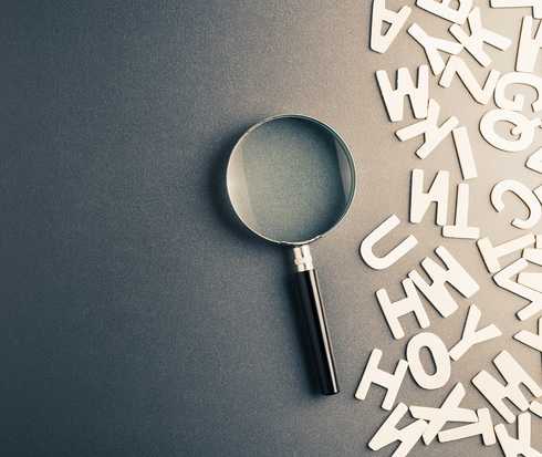 Eine Lupe liegt neben vielen verschiedenen Buchstaben