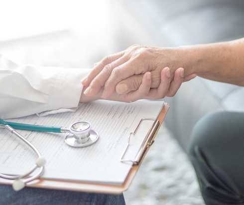 Ein Arzt und ein Patienten halten sich stärkend an den Händen