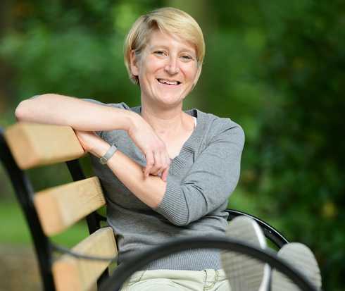 Patientin Franziska sitzt auf einer Parkbank und lacht in die Kamera