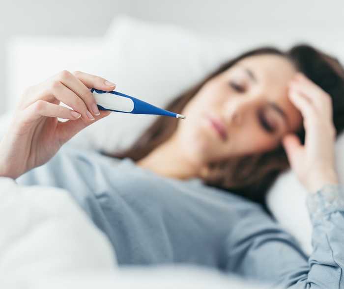 Eine Frau liegt im Bett und schaut auf ein Fieberthermometer