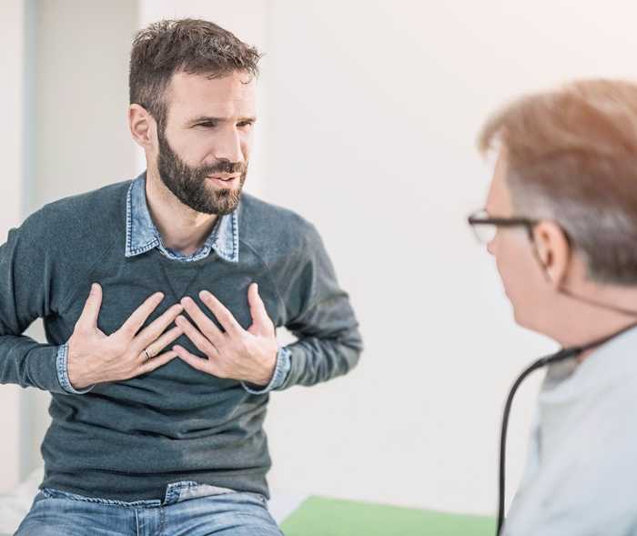 Ein Mann sitzt beim Arzt und hält sich die Brust