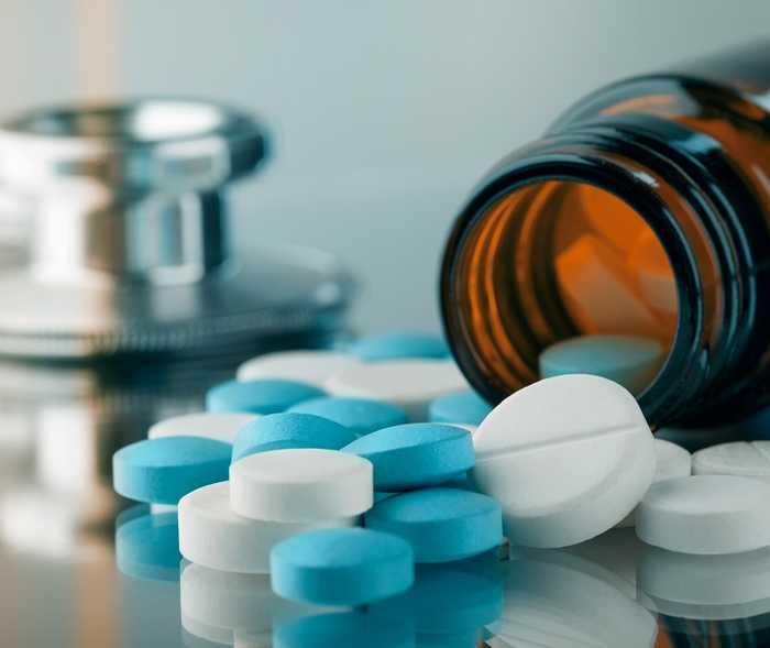 Foto von einem liegenden, geöffneten Arzneimittelbehälter, vor dem blaue und weiße Tabletten liegen