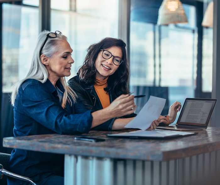 Zwei Frauen schauen sich auf einem Papier etwas an und die eine Frau zeigt mit einem Stift darauf