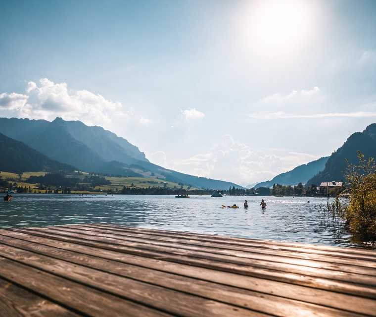 Ausblick von einem Holzsteg auf einen Badesee in den Bergen