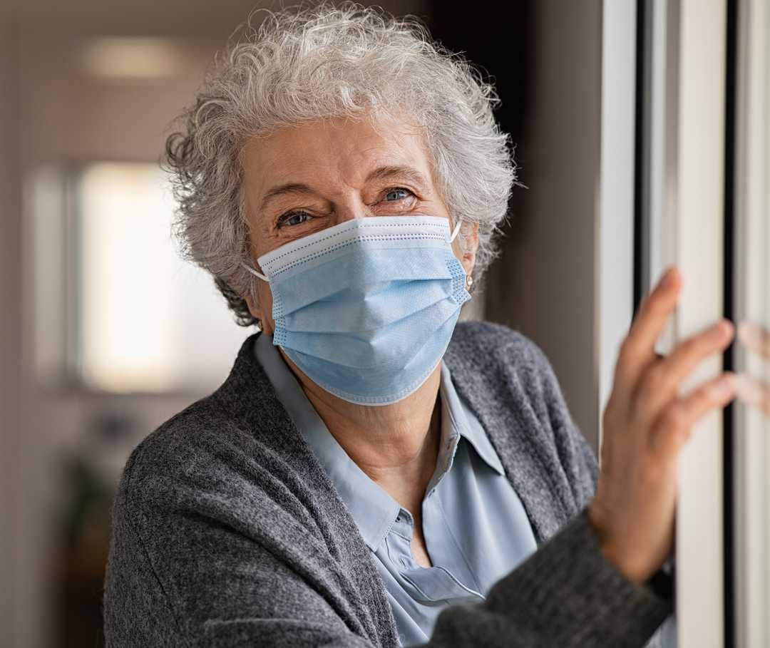 Eine Dame mit medizinischer Maske schaut freundlich in die Kamera